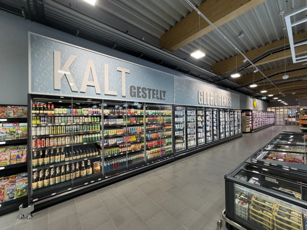Kühlregalzeile unter dem Wandschriftzug »Kalt gestellt« mit Blick durch die Ladenpassage