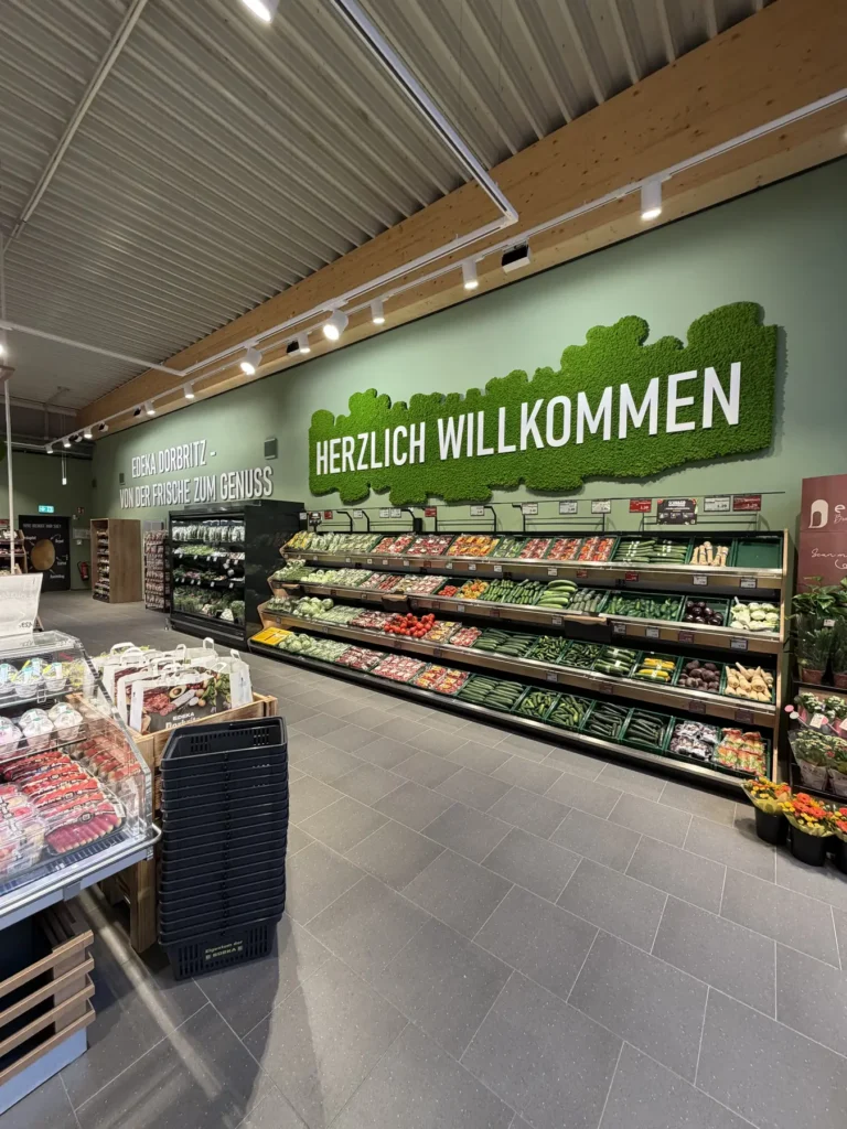 Obst- und Gemüseregal mit Wandschriftzug »Herzlich Willkommen« am Eingang