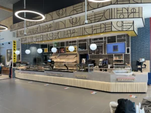 Bedientheke mit Brotregal unter geometrischer Bauhaus-Wandgrafik, EDEKA-Bildschirm im Hintergrund
