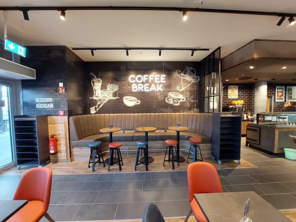 Polsterbank mit Stehtischen vor der Wandgrafik »Coffee Break«
