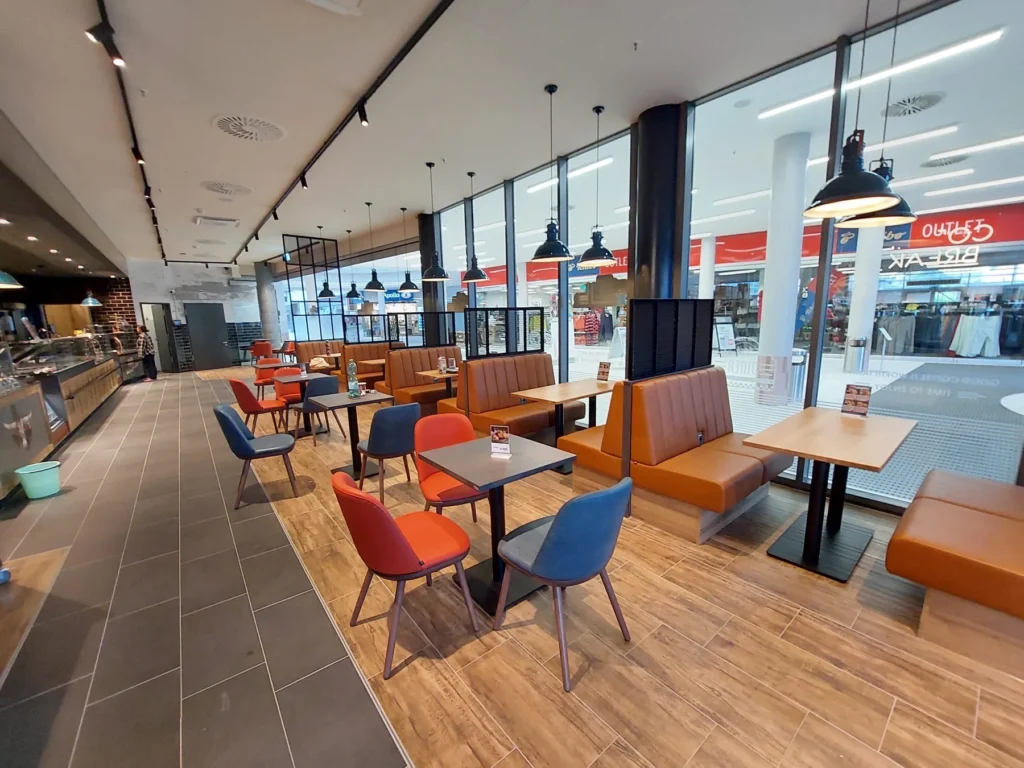Sitzbereich mit Polsterbänken und Holztischen an der Glasfront zur Ladenpassage