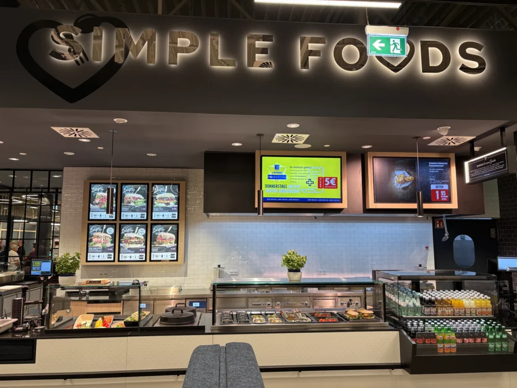 Imbisstheke unter dem Schriftzug »Simple Foods« mit Menütafeln und Getränkekühlung