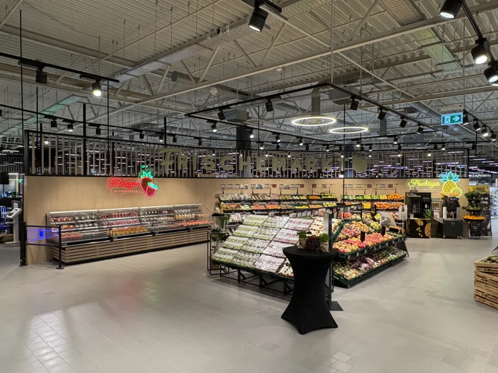 Frischemarkt mit Obst- und Gemüsetischen, Kühlregal und Leuchtschriften
